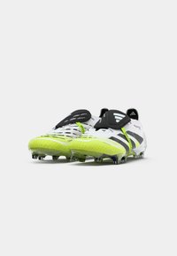 Een paar witte en neongele Adidas Predator voetbalschoenen met zwarte klittenbandsluitingen en noppen op de zolen, schuin naar voren op een witte achtergrond.