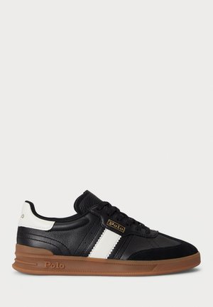 Sneaker in pelle nera con strisce bianche, suola marrone e branding Polo sul lato e sul tallone, mostrato dal lato esterno.
