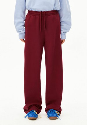 Bordeauxrode joggingbroek met een elastische tailleband en trekkoord, voorzien van een comfortabele pasvorm en een logo aan de zijkant, gecombineerd met blauwe sneakers.