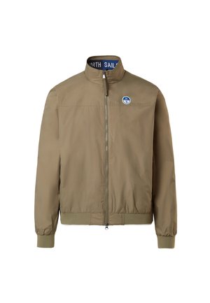 Giacca bomber color khaki con colletto alto, zip frontale, polsini e vita a costine. Presenta un logo rotondo blu sul lato sinistro del petto.