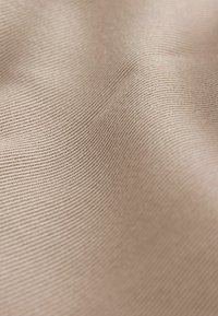 Tissu beige texturé avec de fines rayures horizontales, surface douce et lisse, présentant de subtiles ondulations et plis.