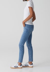 Jeans de mezclilla de color azul claro con un corte ajustado, combinados con una camisa de manga corta blanca y zapatillas blancas con rayas en azul marino y suela de goma.