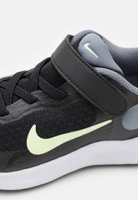 Chaussure de sport noire avec tige en maille, accents gris et swoosh vert lime. Dotée d'une bande Velcro et d'un col rembourré pour un soutien optimal.