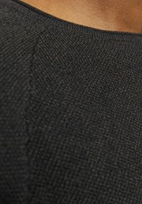 Tessuto a maglia nera con una superficie testurizzata, caratterizzato da un collo rotondo e dettagli di cucitura visibili. Primo piano di un dettaglio del capo.