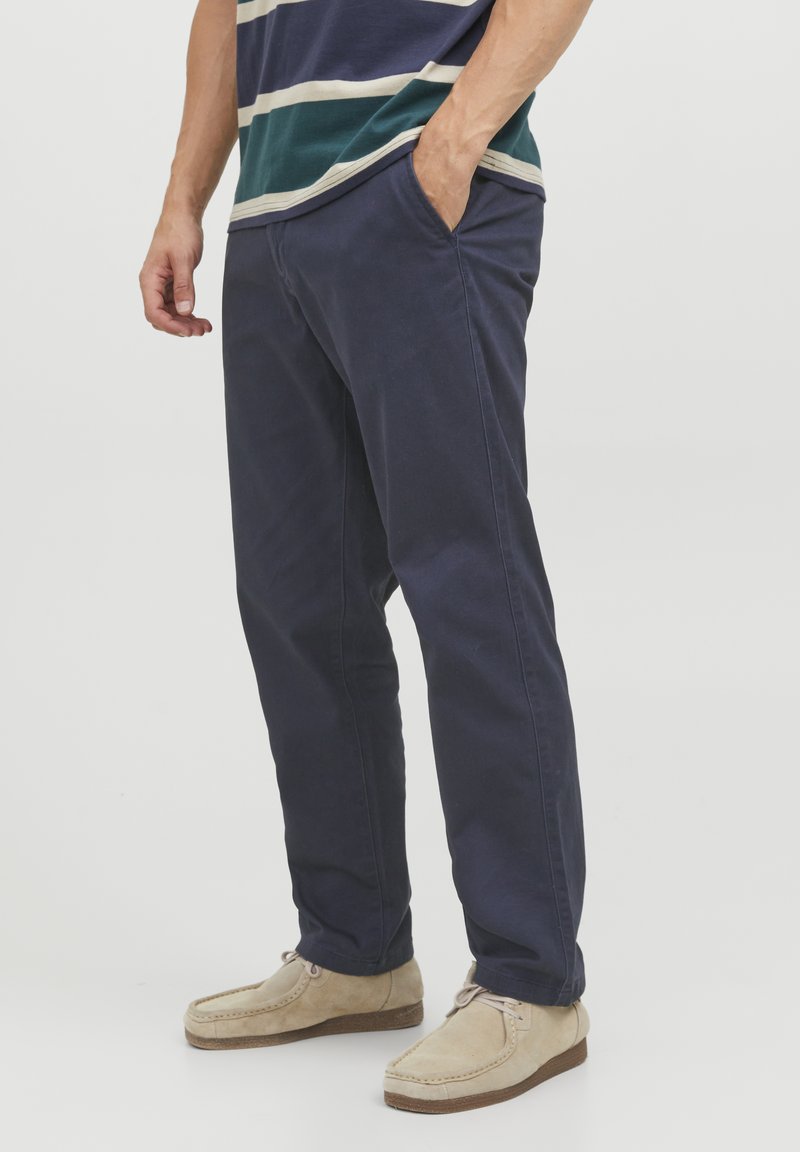 Pantalons en coton bleu marine avec poches latérales, design à jambe droite et texture subtile ; assortis à des chaussures décontractées beiges.