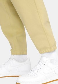 Pantaloni de trening galbeni deschis cu manșete elastice, asortați cu adidași albi și șosete albe texturate. Adidașii au o talpă din cauciuc și o marcaj subtil.