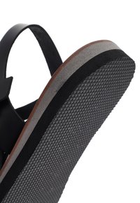 Black sandal with a textured rubber sole and a wooden insole. Features a smooth strap and a curved design for comfort.
