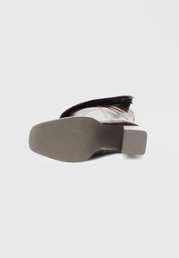 Bota de couro castanha com bico arredondado, sola texturizada e salto baixo em bloco. O design apresenta seções lisas e ligeiramente enrugadas.