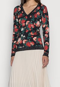 Blommig långärmad topp med svart bas och röda och vita rosor, V-ringning och glittrande kant vid ärmsluten och nederkanten.