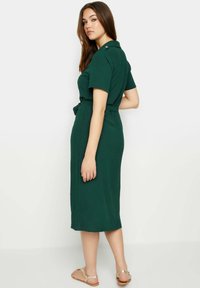 Robe midi verte avec des manches courtes et une taille ceinturée. Fabriquée en tissu texturé, elle présente des détails de boutons au col.
