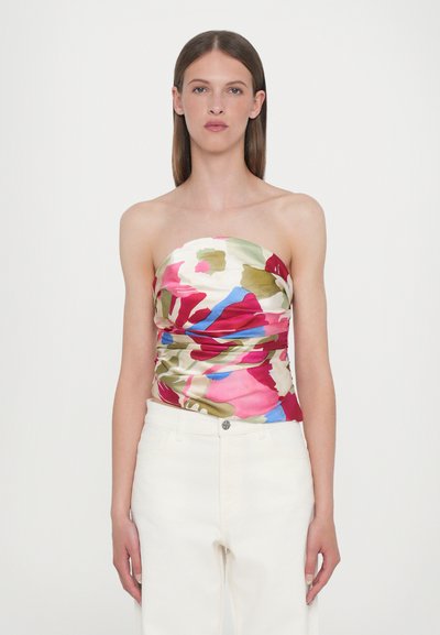 Blumiges, trägerloses Oberteil mit lebendigen Mustern in Pink, Grün und Blau, gerafftem Stoff und einer glatten, glänzenden Textur. Kombiniert mit weißen Hosen.