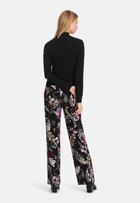 Schwarzer Rollkragenpullover kombiniert mit weitgeschnittenen, floralen Hosen in Schwarz, Pink und Grün. Glatte Textur, minimalistisches Design und lebendige Musterdetails.