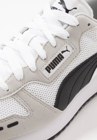 Kengät, joissa on harmaa nubuk- ja verkko-yläosa, valkoiset nauhat, mustat yksityiskohdat ja suuri PUMA-logo sivulla.