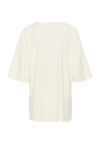 Oversized krämfärgad t-shirt med korta ärmar, rund halsringning, mjukt bomullsmaterial och slät yta. Bakom ser vi en jämn fåll.