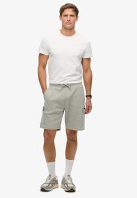 Lichtgrijze cargoshorts met zijzakken, elastische tailleband en trekkoord. Gecombineerd met een strak wit T-shirt en grijze sneakers.
