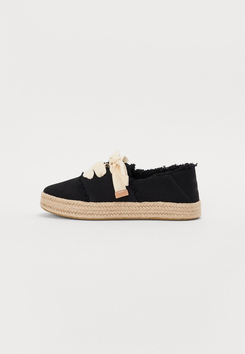 Chaussure décontractée noire avec une semelle beige tissée épaisse et des lacets rubans couleur crème, avec des bords de tissu effilochés et un design à coupe basse.