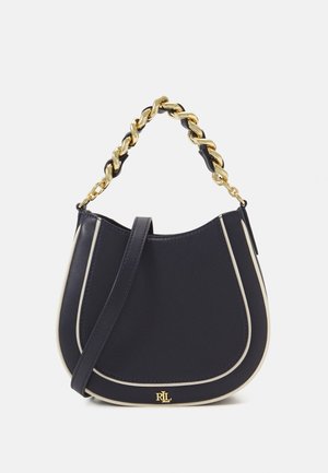 Marineblauwe handtas met crème accenten, met een gebogen silhouet, een goudkleurige kettinghendel en een afneembare schouderriem. Gouden logo aan de onderkant.