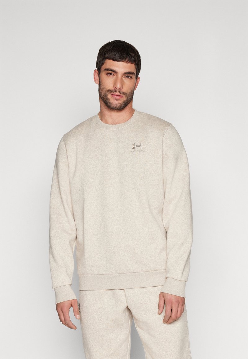 Sudadera beige clara con cuello redondo, mangas largas y puños acanalados. Presenta un pequeño logo bordado en el pecho. Textura suave.