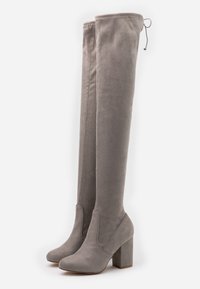 Botas de gamuza gris por encima de la rodilla con un tacón de bloque. Presentan una textura suave, puntera redondeada y una parte superior ajustada con acento de cordón.