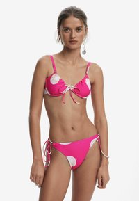 Roze bikini met wit schelp patroon; verstelbare banden aan de bovenkant en zijkanten; zachte stof met een gladde textuur.