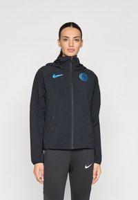 Black Nike jacket with a high collar, full zipper, and blue logo. Features two side pockets and lightweight fabric with a textured finish.