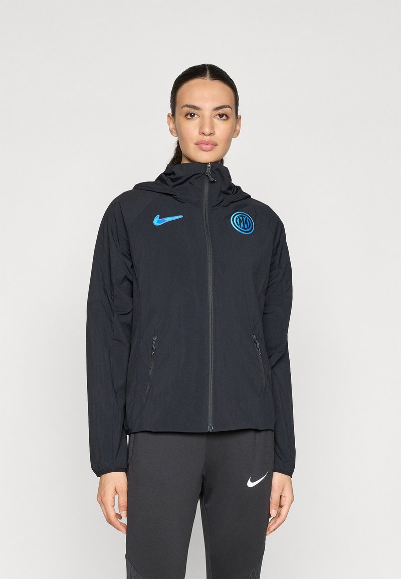 Black Nike jacket with a high collar, full zipper, and blue logo. Features two side pockets and lightweight fabric with a textured finish.