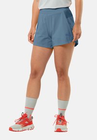 Blauwe lichtgewicht shorts met een gladde textuur, voorzien van zijzakken en een ontspannen pasvorm, gecombineerd met grijze sokken en schoenen met rode accenten.