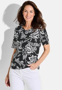 Zwart bloemenpatroon kortmouwtop met witte ontwerpen, voorzien van een ronde halslijn en subtiele textuur, gecombineerd met witte broeken.