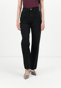 Sorte høye jeans med rett ben-design, som har knappelukking, sidelommer og en subtil tekstur. Komplimentert av beige sko.