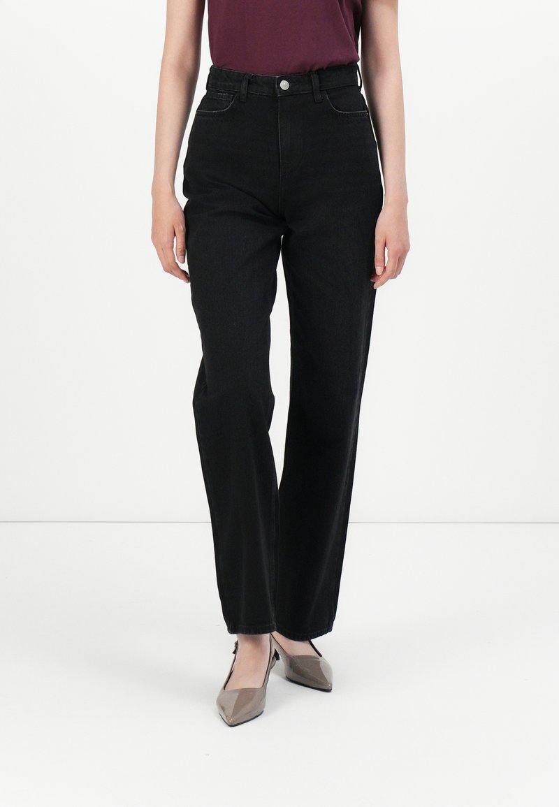 Sorte høye jeans med rett ben-design, som har knappelukking, sidelommer og en subtil tekstur. Komplimentert av beige sko.