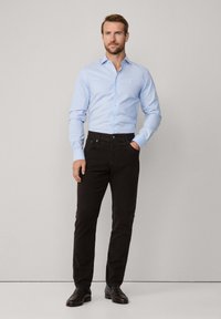 Camisa de botones azul claro de manga larga, combinada con jeans negros de corte Slim y zapatos de vestir oscuros. Diseño minimalista con líneas limpias.