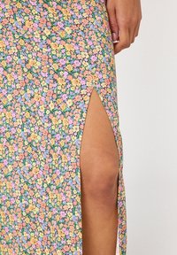 Kukudha na maua ya rangi ya rangi ya rangi ya machungwa, njano, na zambarau, na kwamba kuna tundu la juu la thigh, likionyesha ngozi iliyofichuliwa na mkono ukilipumzika karibu na tundu hilo.
