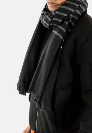 Hombre vestido con un abrigo negro y una bufanda gruesa de rayas negras y grises alrededor del cuello.