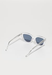 Ochelari de soare tip cat-eye, cu lentile de un albastru închis și rame transparente subțiri. Formă unghiulară distinctivă și finisaj neted pe brațe.