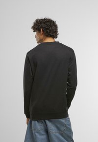 Melnas garām piedurknēm sporta krekliņš ar apaļu kakla izgriezumu un ribotām aprocēm. Gluda tekstūra, brīvs piegriezums un minimāls apdare aizmugurē.