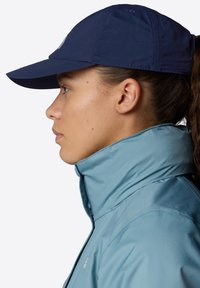 Light blue zip-up jacket with high collar and textured fabric, paired with a dark blue cap, shot from the side. No visible embellishments.