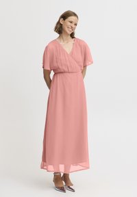 Robe longue et fluide en tissu léger et transparent rose pâle. Présente un décolleté en V et des manches courtes. Associée à des escarpins argentés à bout pointu.