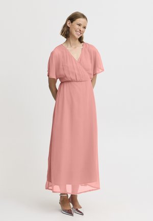 Langes, fließendes Kleid aus transparentem, hellrosa Stoff. Es hat einen V-Ausschnitt und kurze Ärmel. Kombiniert mit silbernen, spitzen Pumps.