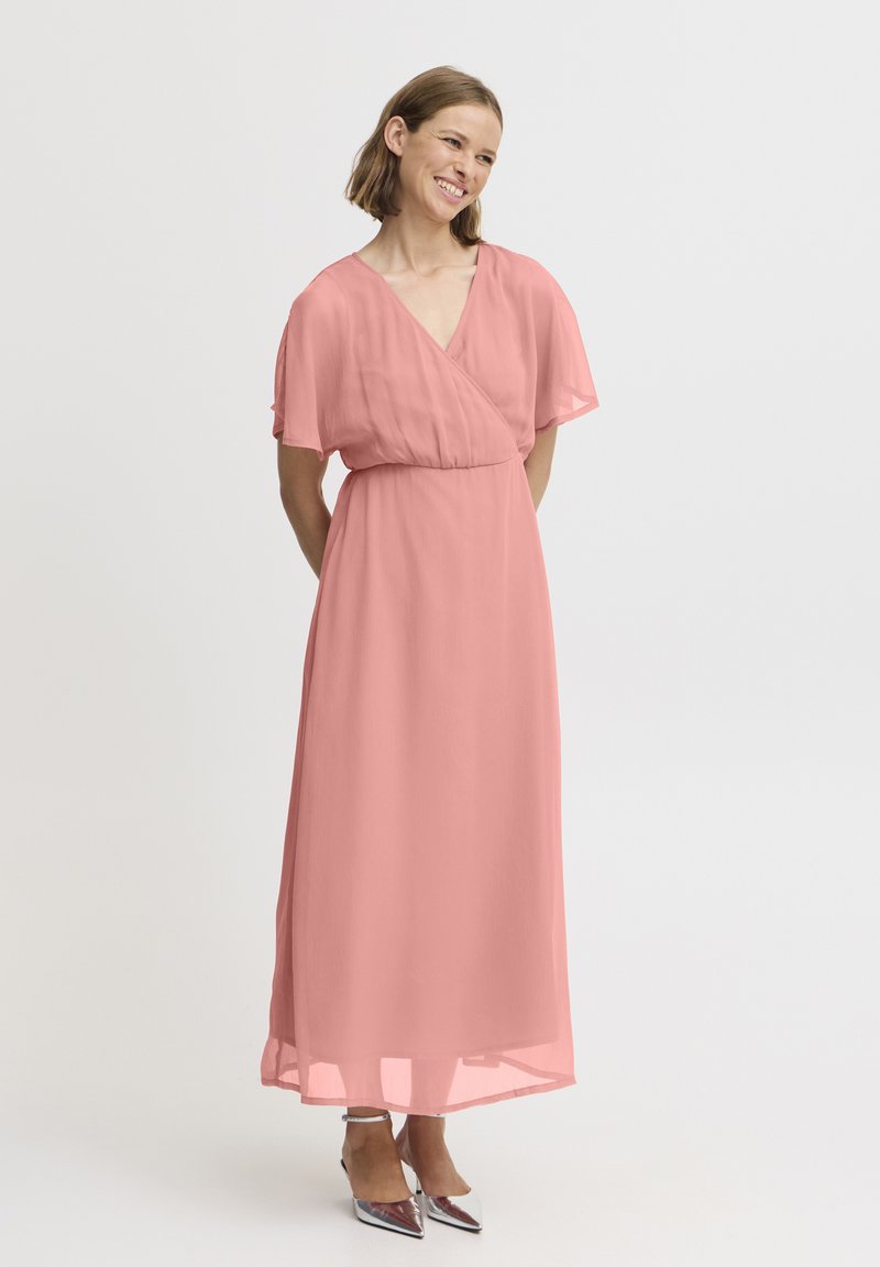 Robe longue et fluide en tissu léger et transparent rose pâle. Présente un décolleté en V et des manches courtes. Associée à des escarpins argentés à bout pointu.