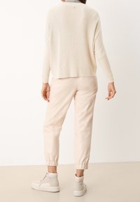 Lichtbeige gebreid sweater, losse pasvorm, geribde textuur. Gecombineerd met zachte roze leren joggers, elastische mouwen en lichtbeige high-top sneakers.