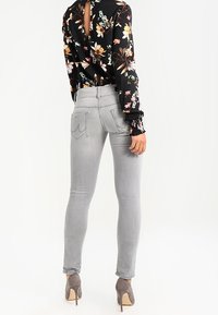 Jean skinny gris avec surpiqûres sur les poches arrière, assorti à un chemisier noir à fleurs avec une découpe dans le dos et des manches ajustées. Chaussures à talons hauts.