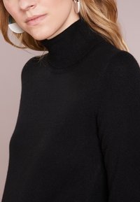 Czarny sweter z golfem wykonany z miękkiej dzianiny, z dopasowanym kołnierzem i rękawami raglanowymi dla bezszwowego wyglądu.