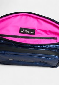 Marineblauwe gevoerde tas interieur met een felroze voering. Beschikt over een zwart label met witte tekst en een ritssluiting. Gladde textuur.