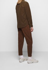 Camisa de pana marrón, de corte relajado, con un cuello abotonado. Combinada con pantalones de pana marrones a juego y zapatillas beige.