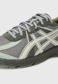 Grey athletic shoe with mesh and synthetic upper, detailed with light green accents and textured design, featuring a padded collar and laces.