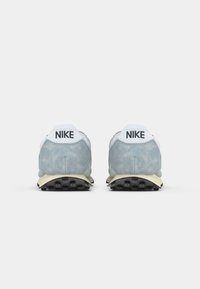 Par svetlo modrih in belih Nike superg, prikazanih od zadaj, z črnimi Nike logotipi na petnem traku in črnimi gumijastimi podplati.