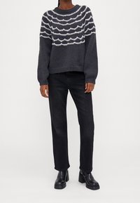 Ciemnoszary sweter dzianinowy z falistymi białymi i jasnoniebieskimi wzorami, w połączeniu z czarnymi dżinsami o prostych nogawkach i masywnymi czarnymi botkami na obcasie.