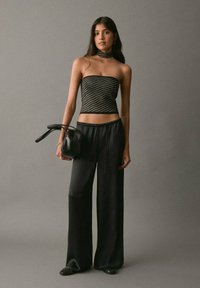 Čierny top bez ramienok s metalickými pruhmi v kombinácii s voľnými čiernymi nohavicami, doplnený malou čiernou kabelkou a kruhovými náušnicami.
