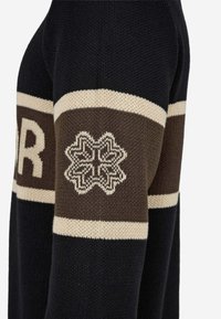 Gestrickter Pullover mit einem marineblauen Körper, der cremefarbene und braune horizontale Streifen sowie ein Schneeflockenmuster am Ärmel aufweist.