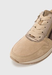 Sneaker beige con tomaia in suede, dettagli testurizzati, design con lacci piatti e zip laterale per un facile accesso.